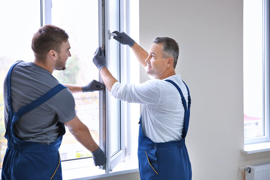 Two male workers installing a thermal glass window whilst wearing gloves