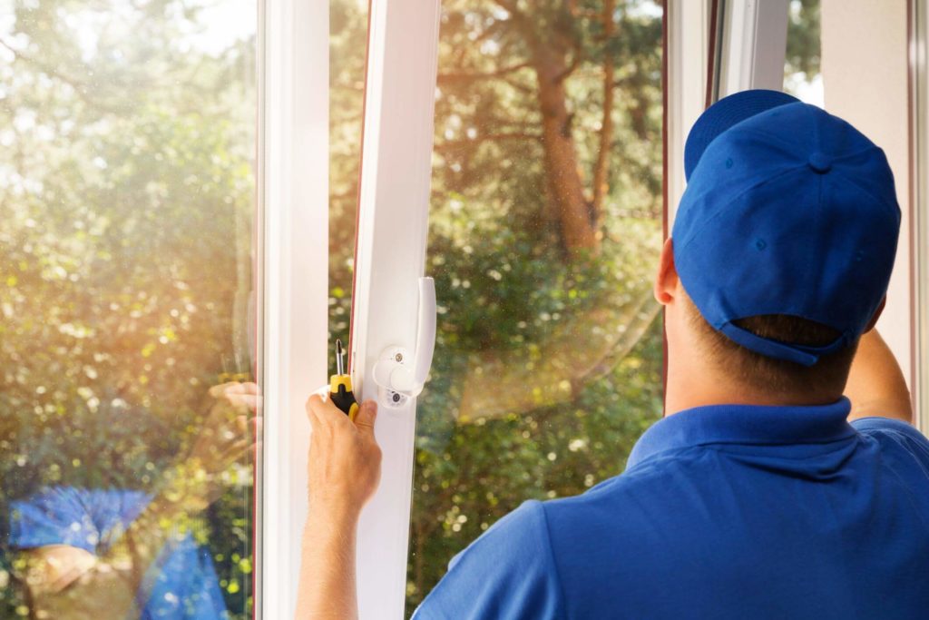 Male worker with a blue shirt and hat putting the finishing touches to a replaced window