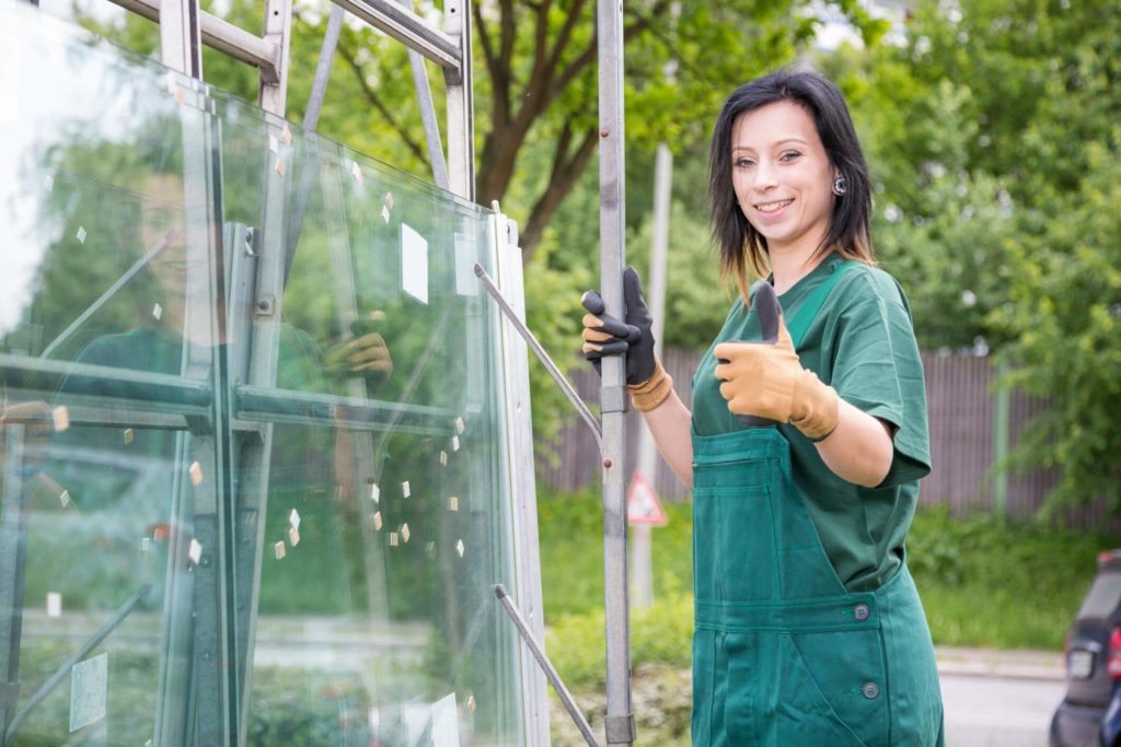 Storefront glass window replacement held by a female worker in green coveralls