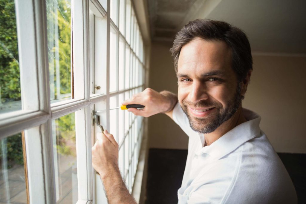 Worker in a white poloshirt putting the final touches to a replaced window with a screwdriver